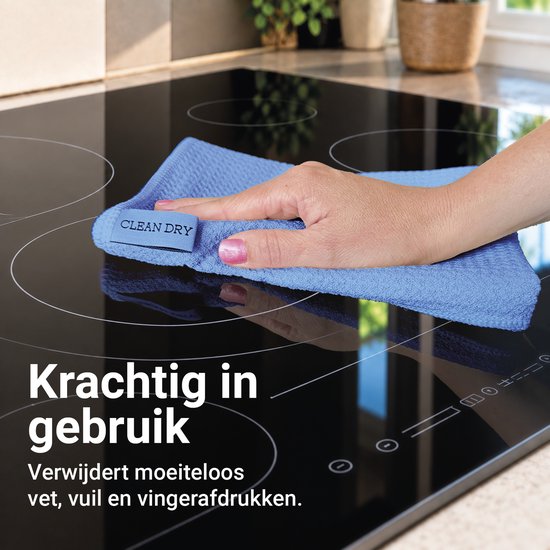 Een hand met een blauwe microvezeldoek van 'Clean Dry' die een glazen kookplaat schoonmaakt.
