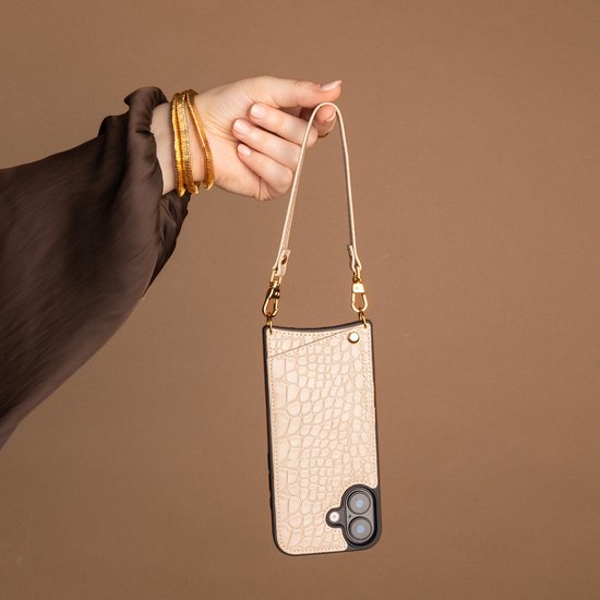 Beige croco-print telefoonhoesje met goudkleurige details en afneembaar polsbandje aan een hand.