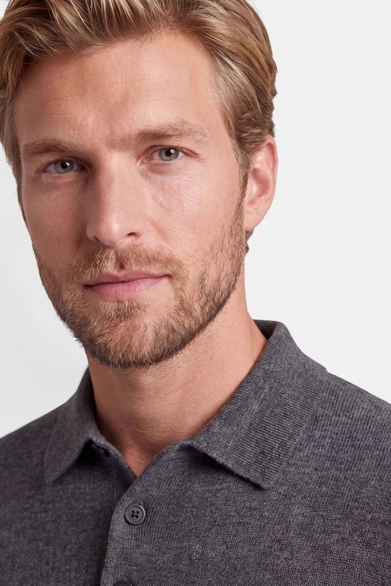 Close-up van een blonde man met baard die een donkergrijze polotrui met knoopsluiting draagt.