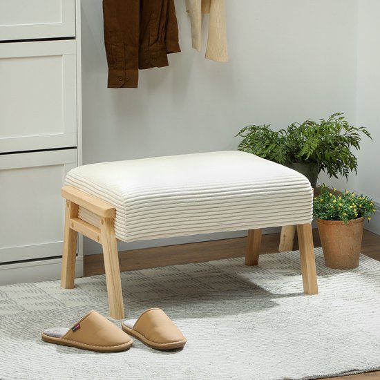 Crèmewit gestoffeerd voetenbankje met corduroy textuur, houten poten en beige slippers op een tapijt.