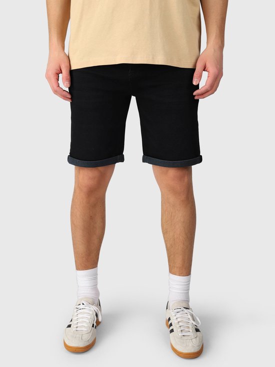 Vooraanzicht van zwarte denim shorts met opgerolde zomen, gedragen door een model in een beige T-shirt.