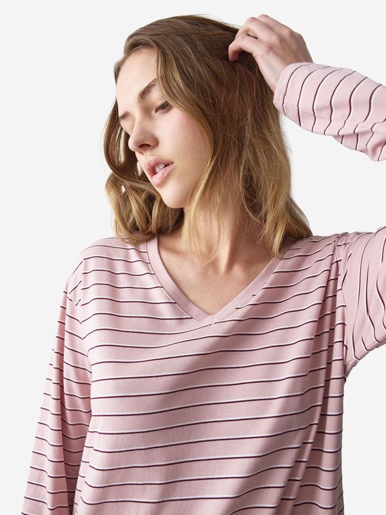 Close-up van model met roze nachthemd met lange mouwen en fijne zwarte streepjes, v-hals. Houdt hand in haar.