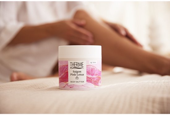 THERME Body Butter pot met roze lotus bloemen en gouden accenten. Vrouw benen op de achtergrond.