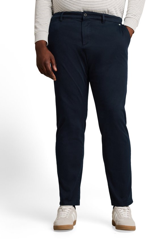 Model draagt een marineblauwe chino met normale pasvorm, gecombineerd met een gestreept shirt en beige sneakers.