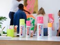Bouteilles de spray néon rose, vert vif et rose d'edding sur une table, avec des œuvres d'art en arrière-plan.