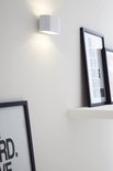 Witte wandlamp met opwaartse lichtstraal, naast ingelijste posters met tekst.