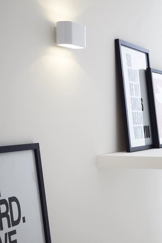 Witte wandlamp met opwaartse lichtstraal, naast ingelijste posters met tekst.