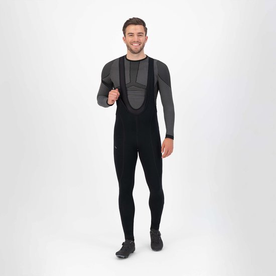 Man draagt een zwarte fietsbroek met bretels en een grijs shirt met lange mouwen. Hij houdt de bretel vast.