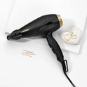 Zwarte BaByliss föhn met gouden details, concentrator, haarspeldjes en sieraden op een witte ondergrond.