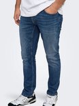 Close-up van de pasvorm van een donkerblauwe slim-fit jeans op een model, gecombineerd met zwart-witte sneakers.