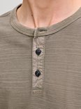 Detailopname van een olijfgroen Henley-shirt met knoopsluiting en wafelstructuur.