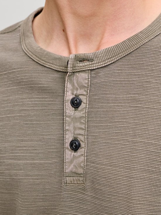 Detailopname van een olijfgroen Henley-shirt met knoopsluiting en wafelstructuur.