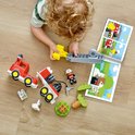 Bovenaanzicht van kind dat met Duplo brandweerauto en handleiding op een houten vloer speelt.