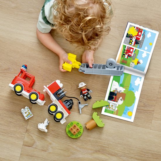 Bovenaanzicht van kind dat met Duplo brandweerauto en handleiding op een houten vloer speelt.