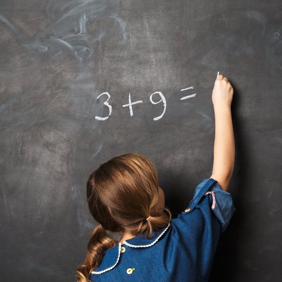 Kind met staartjes schrijft "3+9=" met witte krijt op een schoolbord.