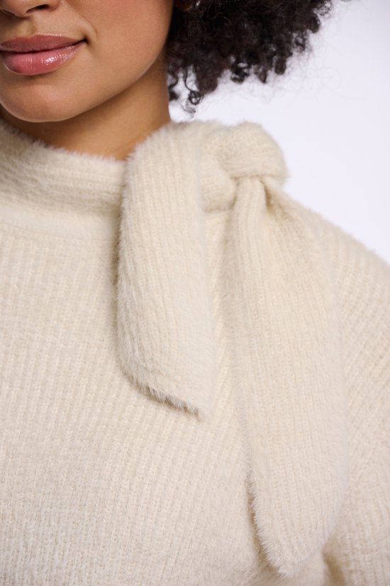Detailopname van een beige gebreide trui met een knoopdetail bij de hals.