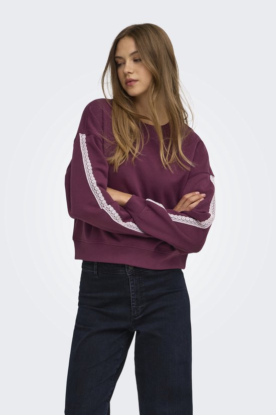 Close-up van een model in een paarse sweater met opvallende witte kanten biezen langs de mouwen.