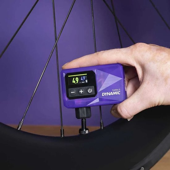 Paarse mini-fietspomp Dynamic Turblo aangesloten op een fietsventiel, met display dat 4.9 PSI en 4.9 BAR aangeeft.