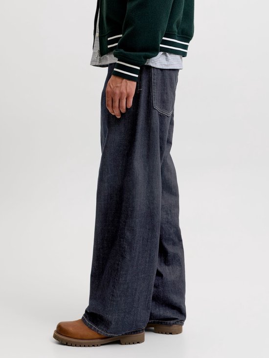 Close-up van de zijkant van een wijde, donkere jeans met contrasterende stiksels en bruine laarzen.