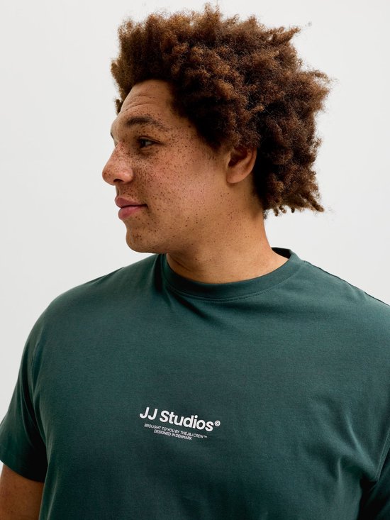 Profiel van een man met krullend haar, gekleed in een donkergroen T-shirt met witte 'JJ Studios' tekst.