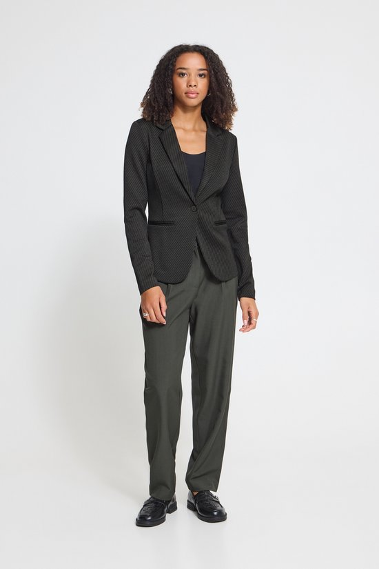 Model in een zwarte blazer met diagonaal patroon, donkergrijze pantalon en zwarte schoenen.