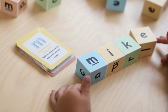 Kleblokken met letters 'm', 'a', 'p', 'i', 'k', 'e' op een houten tafel. Een kaart met de letter 'm' ligt ernaast.
