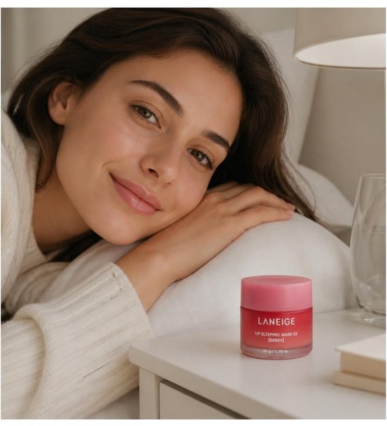 Femme aux cheveux bruns au lit avec le masque de nuit pour les lèvres Laneige Lip Sleeping Mask EX [Berry] sur une table de chevet.