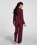 Vrouw met lange donkere haren, gedragen in een pyjamaset in bordeauxrode kleur. Ze staat met de rug naar de camera toe.