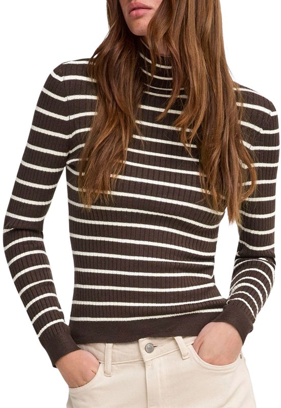 Model met bruine coltrui met witte strepen, gedetailleerd gebreid, en beige broek. Handen in de zakken.