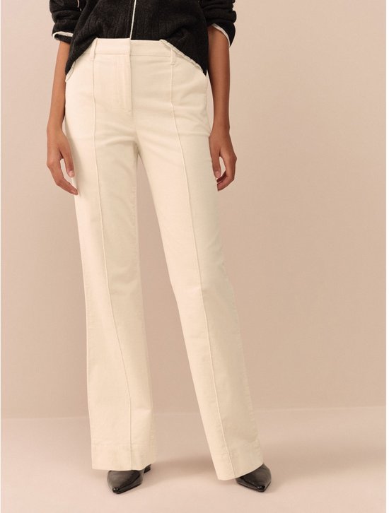 Model in een beige bootcut corduroy broek, focus op de pasvorm bij de benen.