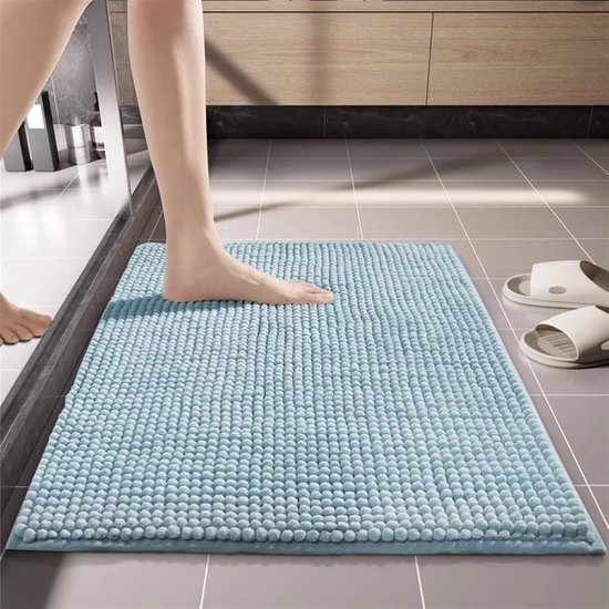 Blauwe badmat met bolletjes textuur, een voet stapt erop in een badkamer.