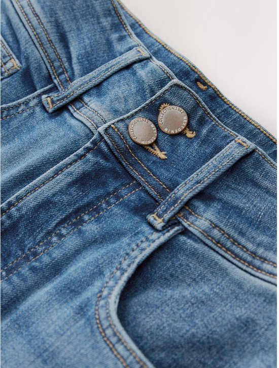 Sluiting van een lichtblauwe jeans met hoge taille, met twee knopen en denim textuur.