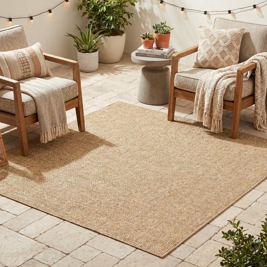 Un tapis d'extérieur beige crème, tissé plat, sur une terrasse avec deux chaises, des coussins et un jeté.