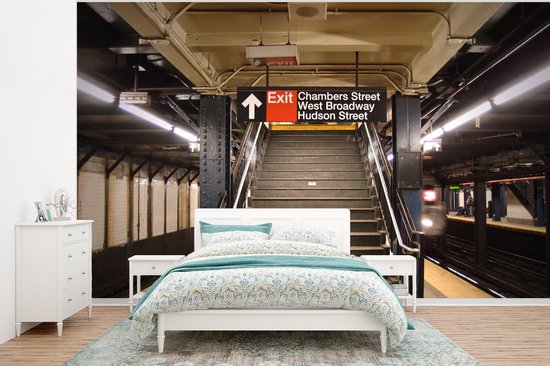 Chambre avec papier peint représentant une station de métro, avec un lit blanc doté de linge de lit bleu et vert.