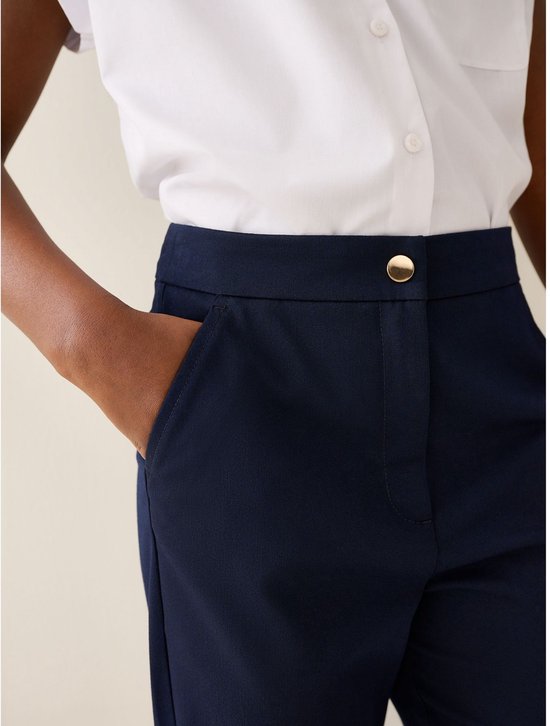 Model met de hand in de zak van een donkerblauwe schoolbroek, met gouden knoop.