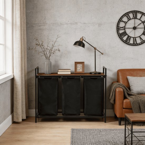 Wasmand met drie zwarte vakken en houten plank, naast een bruine leren fauteuil.