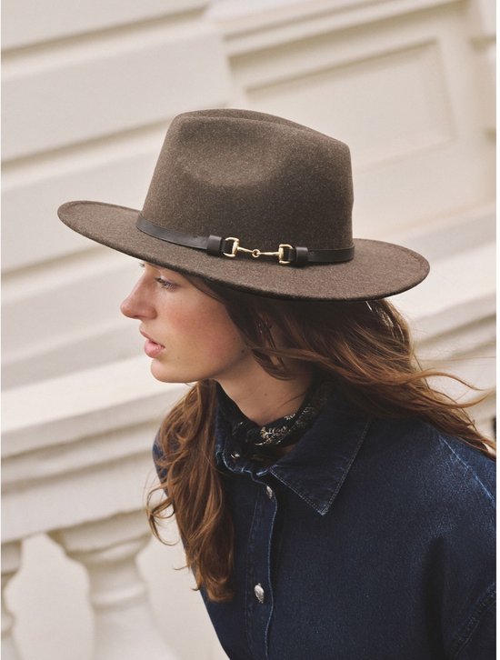 Bruine vilten fedora met zwarte band en gouden bitdetail, gedragen door een model.