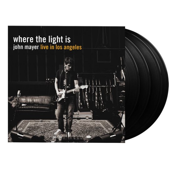 John Mayer op het podium met "where the light is john mayer live in los angeles" hoes, met vier vinylplaten ernaast.
