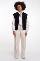 Model in zwart, pluizig gilet, wit overhemd met opengewerkte mouwen en crème broek.
