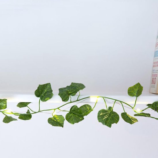 Lichtsnoer met ranken en groene klimopblaadjes op een witte plank.