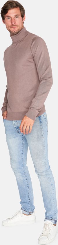 Man met een lachend gezicht draagt een bruine coltrui en een lichte spijkerbroek.