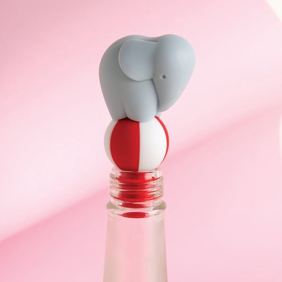 Grijze olifant op een rode en witte bal bovenop een fles, in een roze setting.