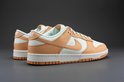 Een paar Nike Dunk Low damesschoenen, wit met oranje overlays, op een grijze achtergrond.