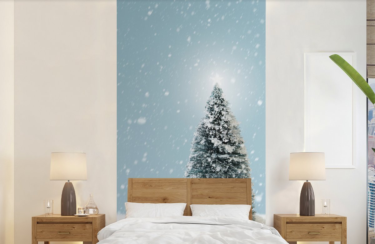 Behang - Fotobehang Een kerstboom in een besneeuwd landschap en een blauwe hemel - Breedte 120 cm x hoogte 240 cm