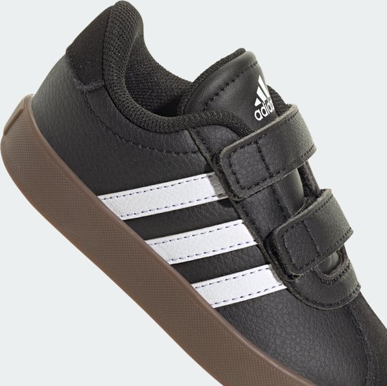 Zwarte Adidas sneaker met witte strepen en klittenbandsluiting, bruine zool.