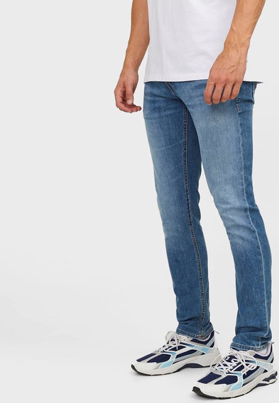 Een man in een lichtblauwe jeans en witte, blauwe en marine sneakers.