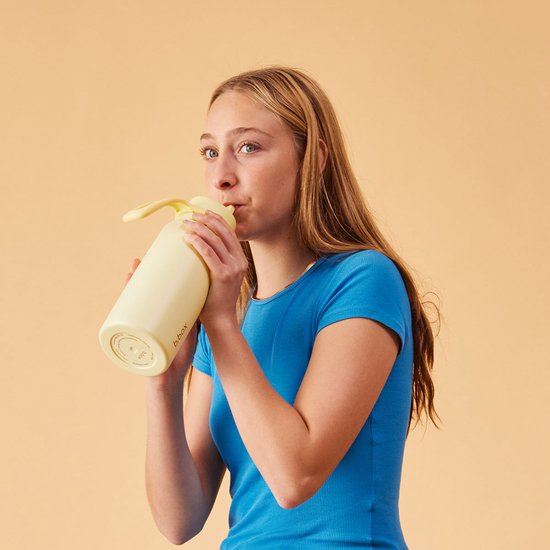 Meisje met lang blond haar in blauw shirt drinkt uit lichtgele b.box fles.