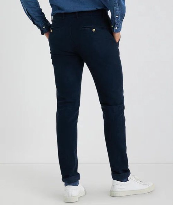 Man, staand, achterkant, draagt donkerblauwe chino broek van McGregor met opgerolde broekspijpen.