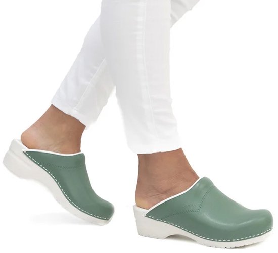 Voeten gedragen in groene Sanita klompen met witte zolen, op een witte achtergrond.