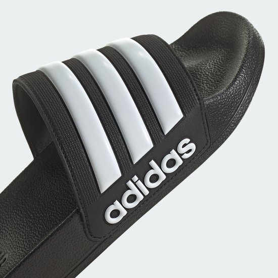 Tongs noires avec bandes Adidas blanches et logo.
